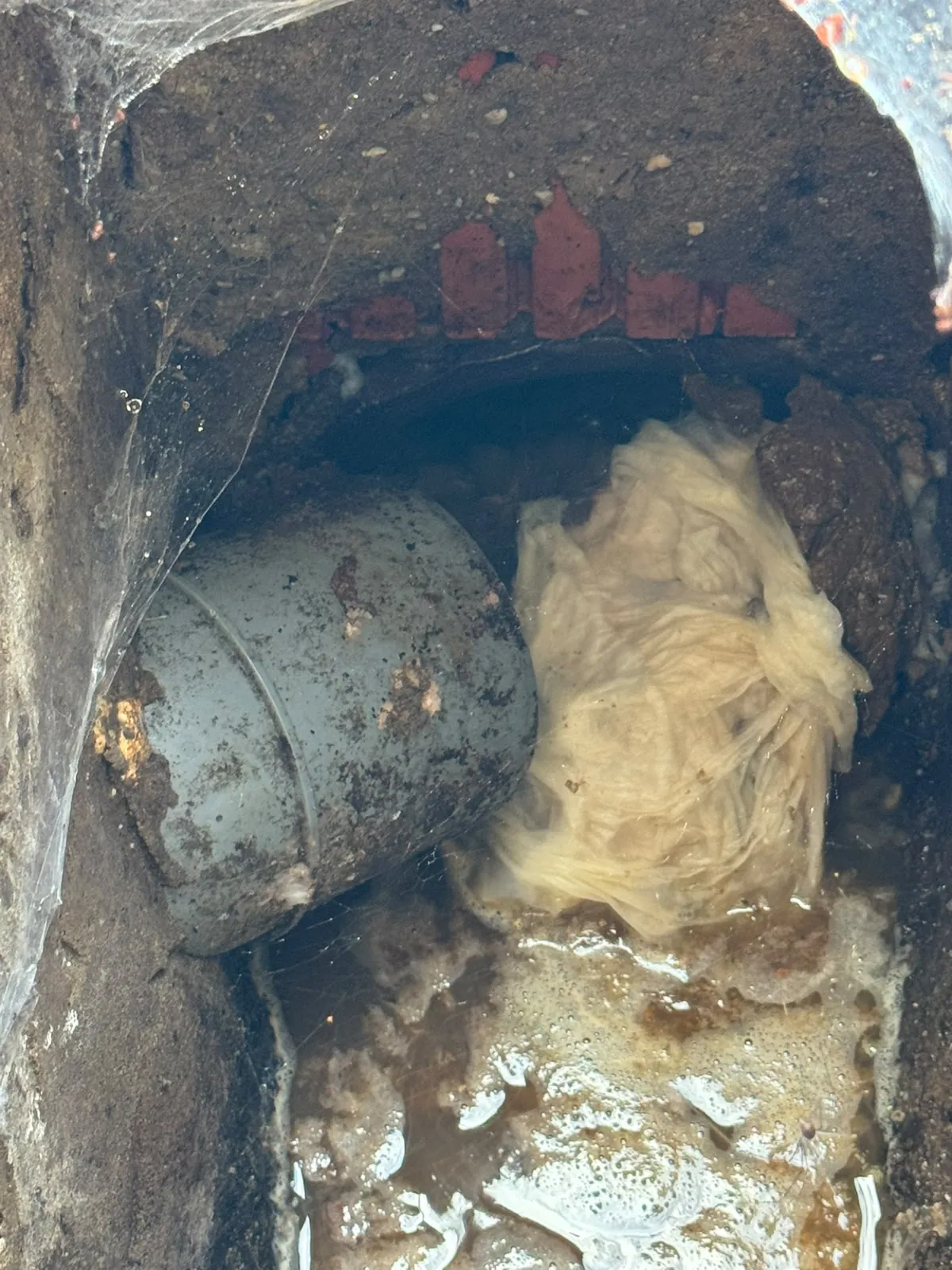 Bouchon de lingettes et de papier sortant d'une canalisation dans une chambre de visite